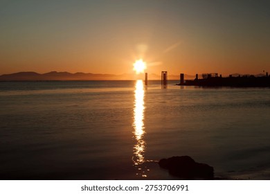 a sun setting over the ocean behind the mountains and the reflection of the sun dances on the water 