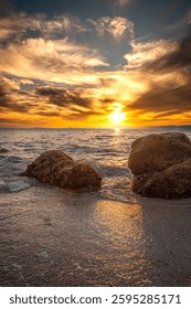 sun setting over the ocean with the sun between shoreline rocks
