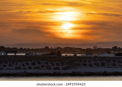 The sun is setting over the ocean, casting a warm glow over the water. The sky is filled with clouds, creating a serene and peaceful atmosphere