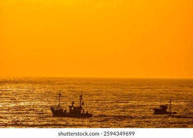 The sun is setting over the ocean, casting a warm glow on the water. A boat can be seen in the distance, and another boat is visible closer to the shore. The scene is peaceful and serene