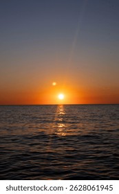 The sun is setting over the ocean, casting a warm glow on the water. The sky is a mix of orange and pink hues, creating a serene and peaceful atmosphere. The water is calm