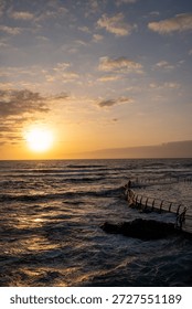 The sun is setting over the ocean, casting a warm glow on the wa
