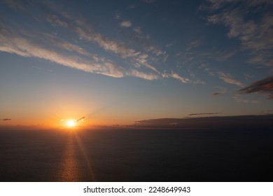  the sun is setting over the ocean on a clear day with a few clouds in the sky and the sun setting over the water with a plane flying in the distance in the distance,. . 