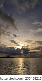 The sun is setting over the ocean on a cloudy day