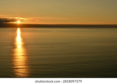 Sun setting over the ocean with sun pillar reflected in calm waters 