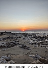Sun setting over the ocean with rocks in foreground