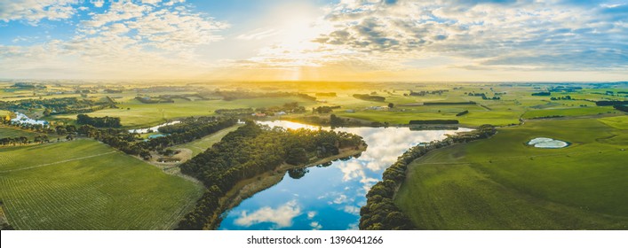 Sun setting over scenic Australian countryside grasslands and pastures with river passing through - aerial panorama