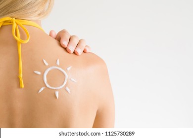 Sun shape created from sunscreen lotion on young woman's back. Skin protection. Safety sunbathing concept. Copy space. Empty place for text on light gray background. 