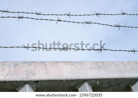 The Sun shines between high metal strong fence with barber wire above. Secure, guarded territory. Very close up photo