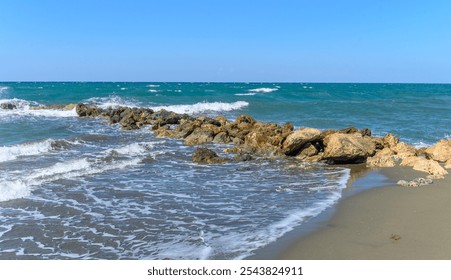 The sun shines brightly as waves gently crash against sunlit rocks along the serene beach coastline. - Powered by Shutterstock