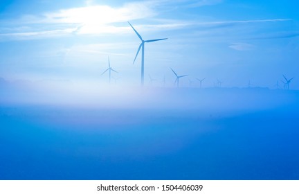 Sun Shines On Wind Turbines In A Foggy Field At Sunrise In Summer