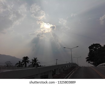 The sun shines through the clouds down the road.
