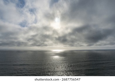 The sun shines through clouds over the Pacific Ocean.