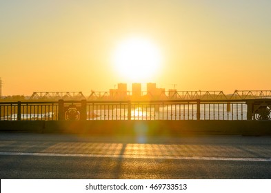 The sun shines through the railing of the bridge at sunset.