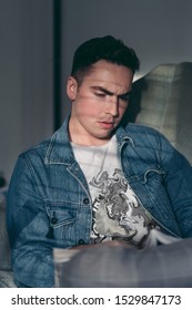 Sun Shines Through The Window Blinds On A Serious Young Man Sitting In A Chair