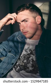 Sun Shines Through The Window Blinds On A Serious Young Man Sitting In A Chair