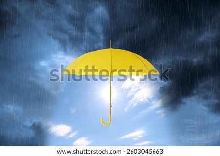 Sun shining in blue sky under open yellow umbrella during heavy rain