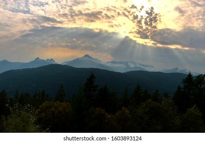 Sun shining through clouds with mountains in the background.
