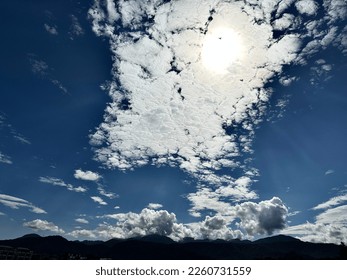 Sun shining through clouds over a mountain.