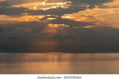 Sun shining through clouds over a calm ocean, creating a beautiful golden reflection on the water at sunrise