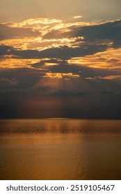 Sun shining through clouds over a calm ocean, creating a beautiful golden reflection on the water at sunrise