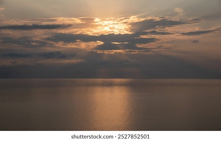 Sun shining through clouds over a calm ocean, creating a beautiful golden reflection on the water at sunrise