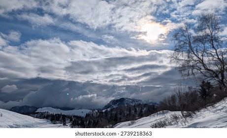 Sun shining through clouds over snowy mountain landscape