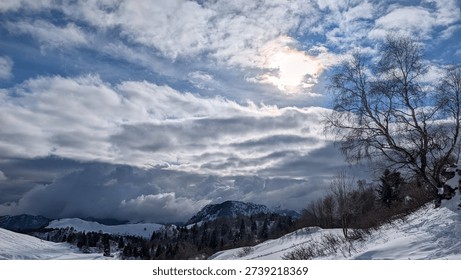 Sun shining through clouds over snowy mountain landscape