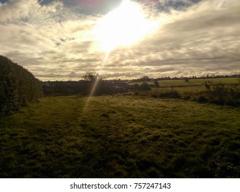 sun shining through clouds over green fields
