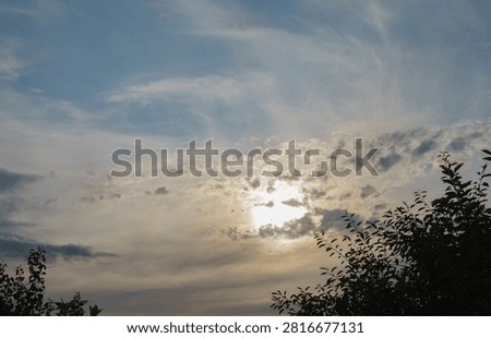 Sun shining through dramatic clouds above treetops, creating a beautiful evening sky landscape.