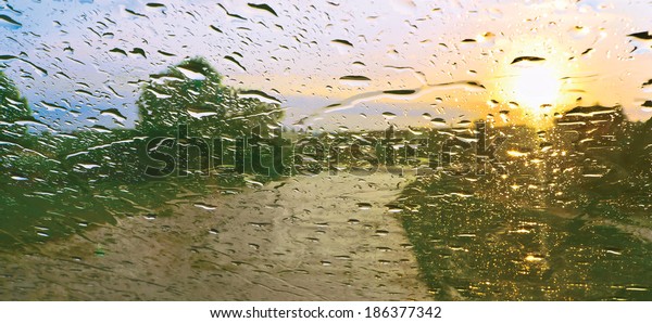 Sun\
shower. Drops of rain on windscreen against\
sunset