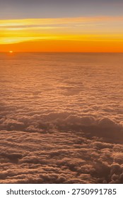 Sun sinks below the horizon while clouds stretch across the sky, creating an orange glow in the background. The view is captured from the window of an airplane flying high. High quality photo