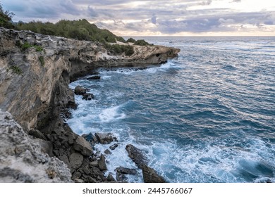 The sun slowly rises over jagged cliffs, which meet the rough turquoise waters of the Pacific Ocean along the Mahaulepu Heritage Trail in Koloa, Hawaii on the island of Kauai. - Powered by Shutterstock