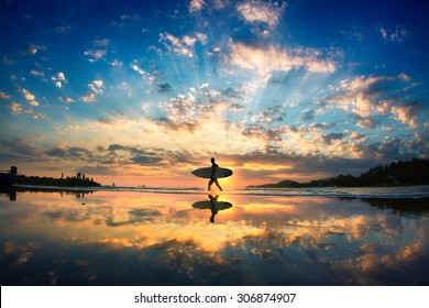 Sun surfer. A man is walking with a surf in his hands across the sea shore.  - Powered by Shutterstock