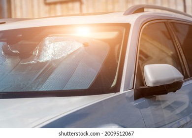 Sun visor or sun reflector on car windshield protects car in parking lot. There is light from sun shining on windshield