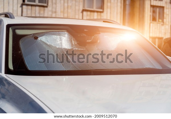 Sun\
visor or sun reflector on car windshield protects car in parking\
lot. There is light from sun shining on\
windshield