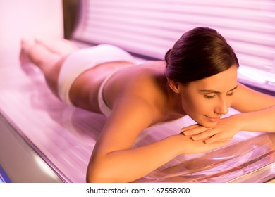 Sunbathing On Tanning Bed. Attractive Young Woman Lying On Tanning Bed And Smiling