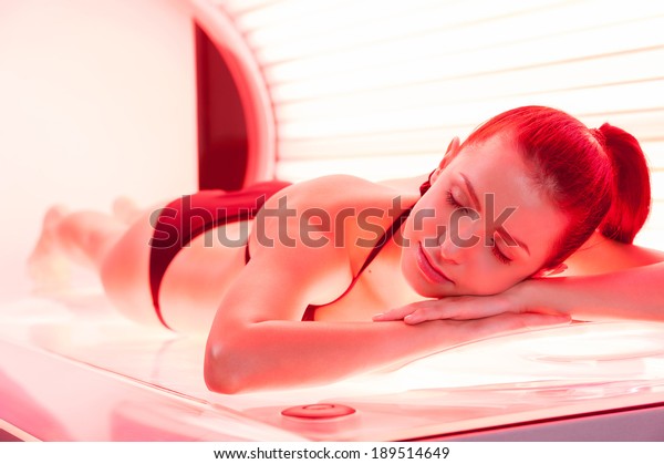 Sunbathing on tanning bed. Beautiful\
young woman lying on tanning bed and keeping eyes\
closed