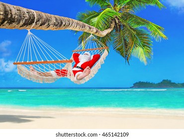 Sunbathing Santa Claus relax in cozy mesh hammock in shadow under coconut palm tree at tropical paradise ocean beach in bright sunny summer day - christmas vacation in hot countries concept - Powered by Shutterstock