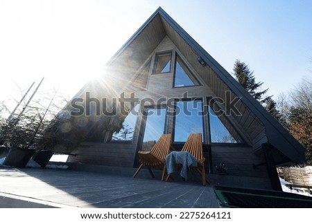Sunbeam terrace of wooden triangle country tiny cabin house in mountains and two chairs. 