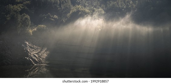 Sunbeams break through wisps of mist floating over the river in Portomarin Galicia