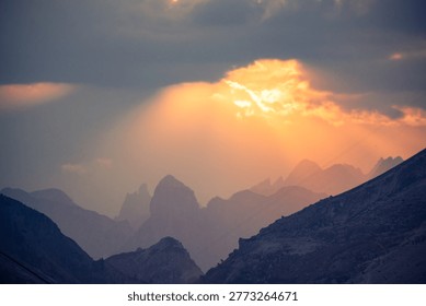 Sunbeams breaking through clouds illuminating a layered mountain range during twilight