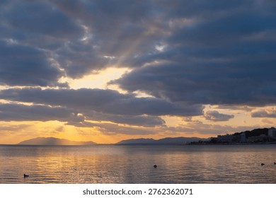 Sunbeams Breaking Through Clouds Over Calm Lake and Mountain Range at Winter Sunset
