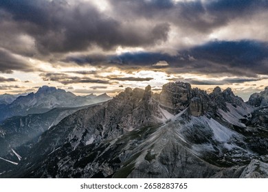 Sunbeams breaking through dramatic clouds over rugged peaks of the Dolomites, highlighting the alpine ridgelines and misty valleys below