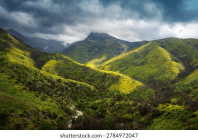 Sunbeams breaking through dramatic clouds over a green mountain valley, creating a scenic natural landscape with soft atmospheric light.