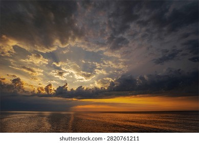 Sunbeams breaking through storm clouds over calm ocean at sunset