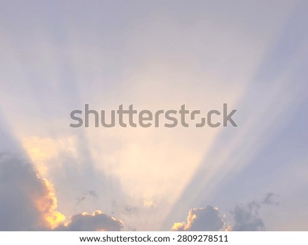 Sunbeams or crepuscular rays breaking through cumulus clouds during a golden sunset sky.