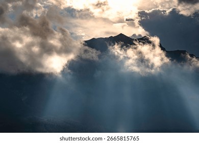 Sunbeams pierce dramatic clouds over majestic mountains and a forest, illuminating a serene landscape, sunbeams breaking through clouds over a mountainous landscape over Canadian Rockies in Canmore