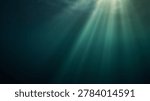 Sunbeams pierce through the surface of deep, dark blue-green ocean water, casting visible light rays into the mysterious and serene underwater environment.