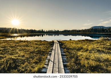 Sunbeams shine over the forest and serene lake in Idre Dalarna, with a wooden walkway inviting exploration during the beautiful Scandinavian summer evening sunset - Powered by Shutterstock